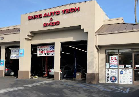 Euro Auto Tech & BMW auto repair shop exterior with a beige facade, open service bays, and signage on a sunny day
