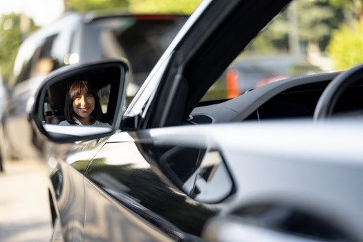 Woman smiling inside of car, reflection on car mirror | Euro Auto Tech & Smog
