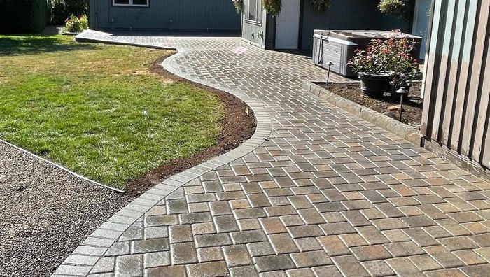 A brick walkway leading to a house with a fence in the background.