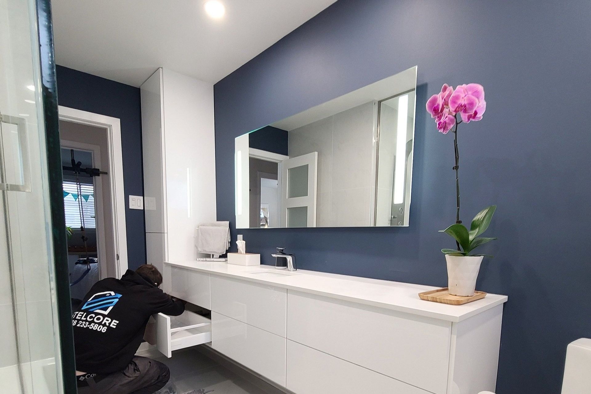 A man is working in a bathroom with a large mirror.