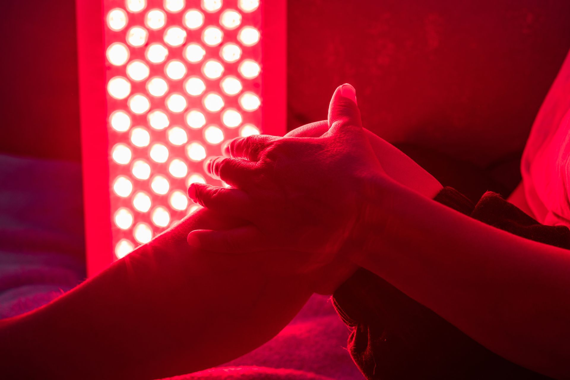 A person's hands massaging a leg under a red light therapy panel.