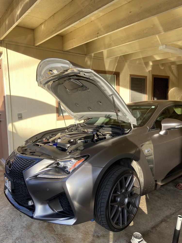 Grey Lexus with its hood open, parked under a carport, likely being worked on.