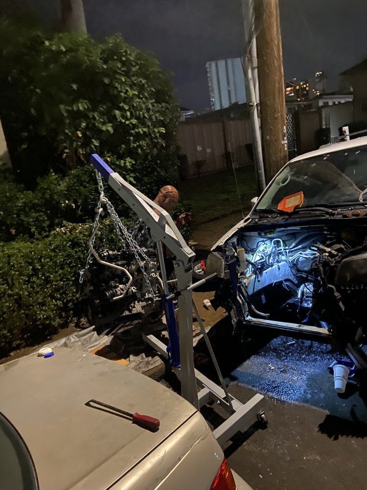 Person working on car engine at night with an engine hoist; in an urban area.