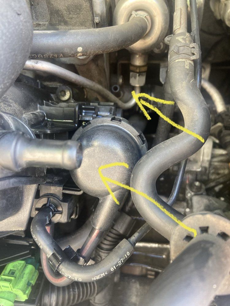 Close-up of car engine parts with yellow arrows pointing to tubes and a black circular component.