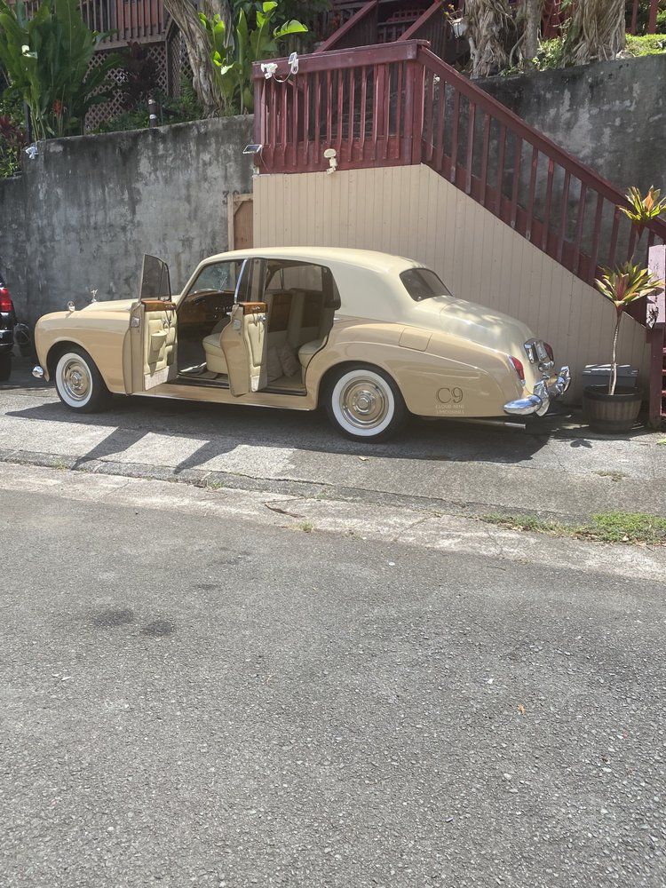 Beige vintage car parked next to a wall and stairs. Doors are open.