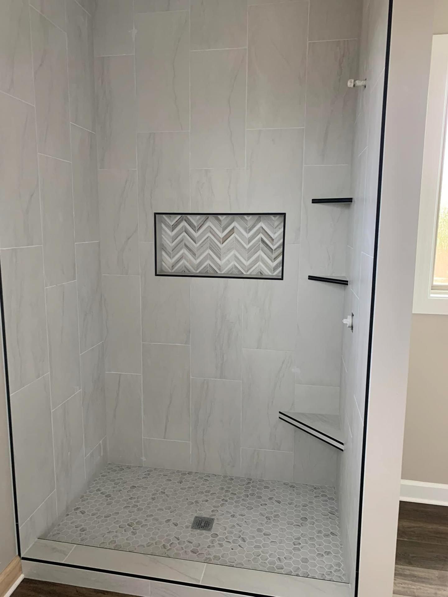 A walk in shower with a glass door and a chevron tile niche.