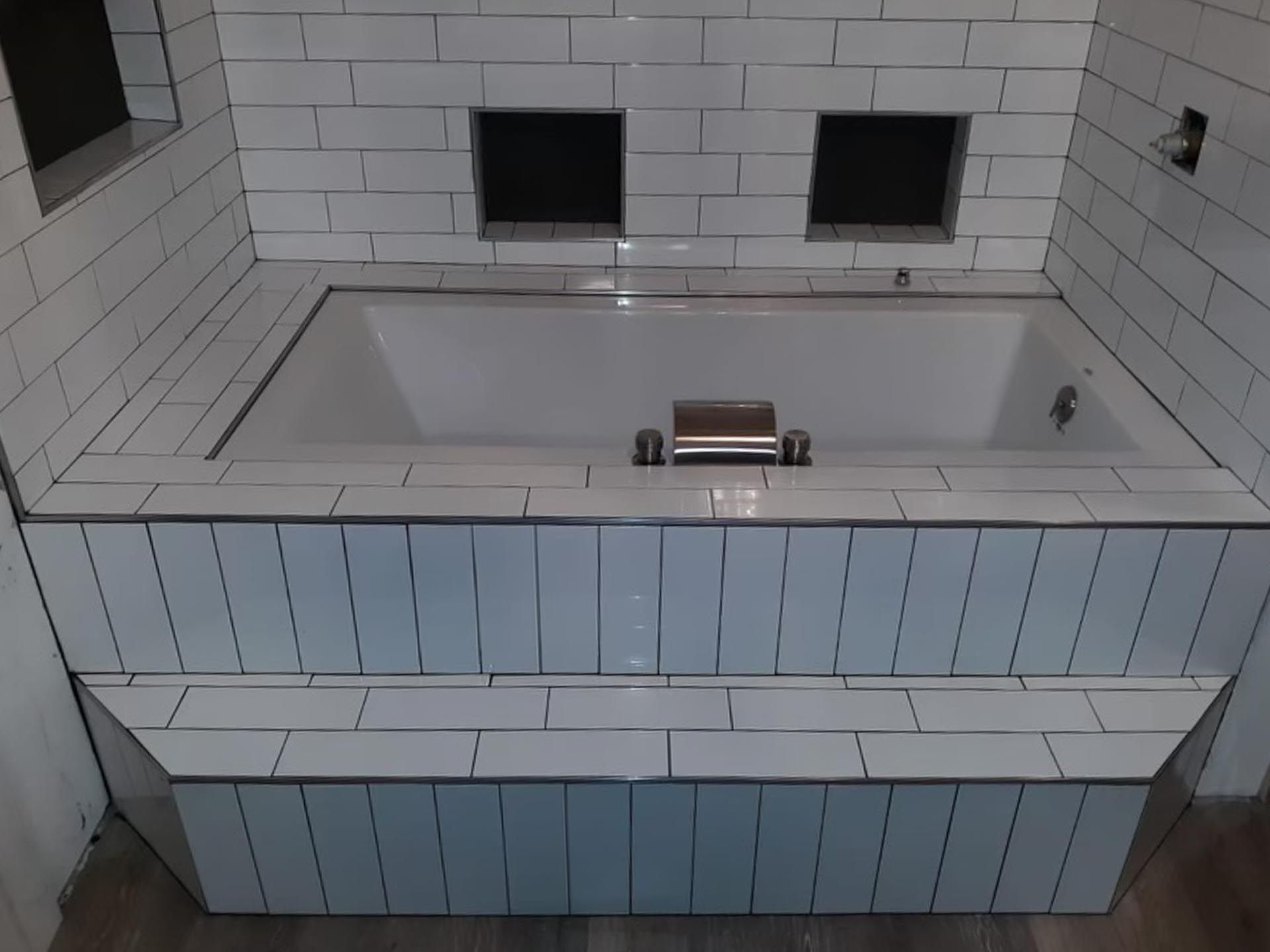 A bathtub is surrounded by white tiles in a bathroom.