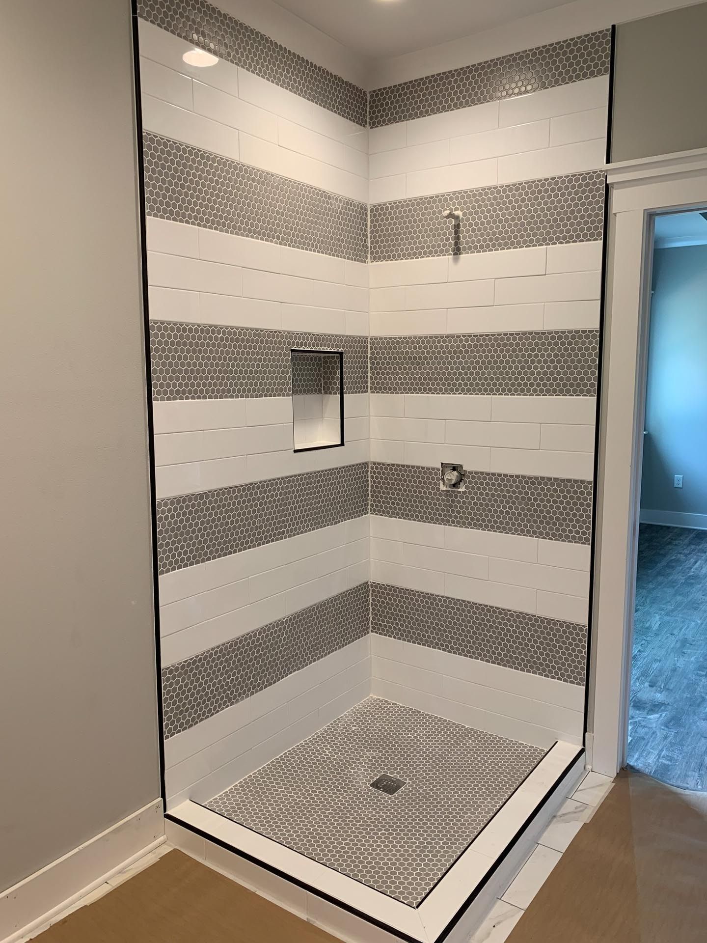 A bathroom with a walk in shower with striped tiles on the wall.