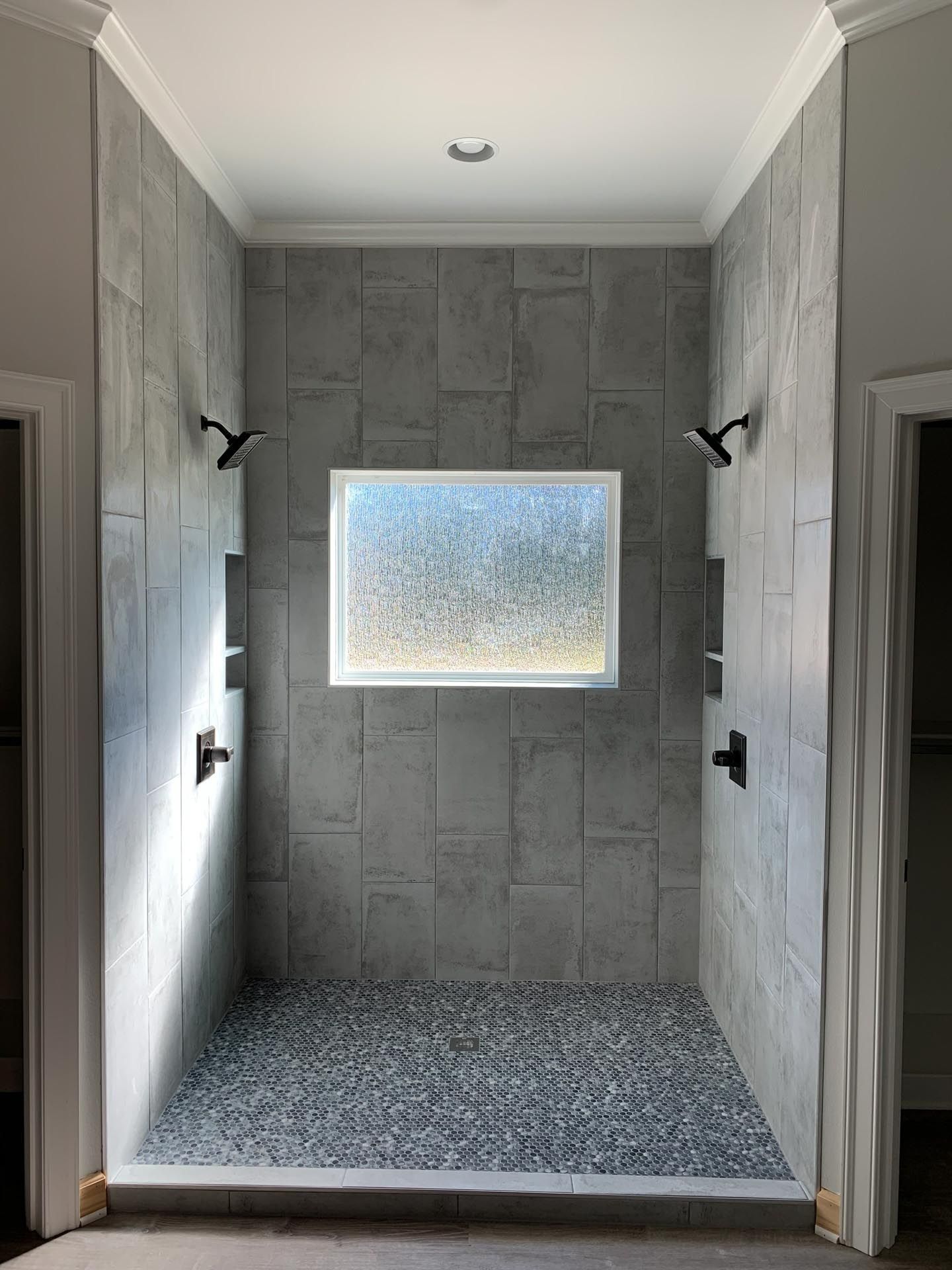 A walk in shower with two shower heads and a window.