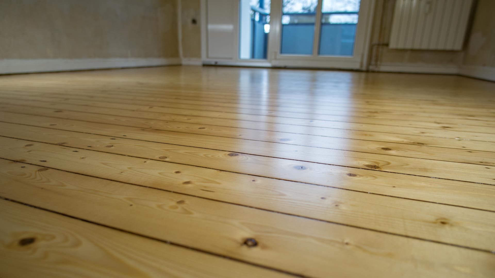 An empty room with a wooden floor and a sliding glass door.