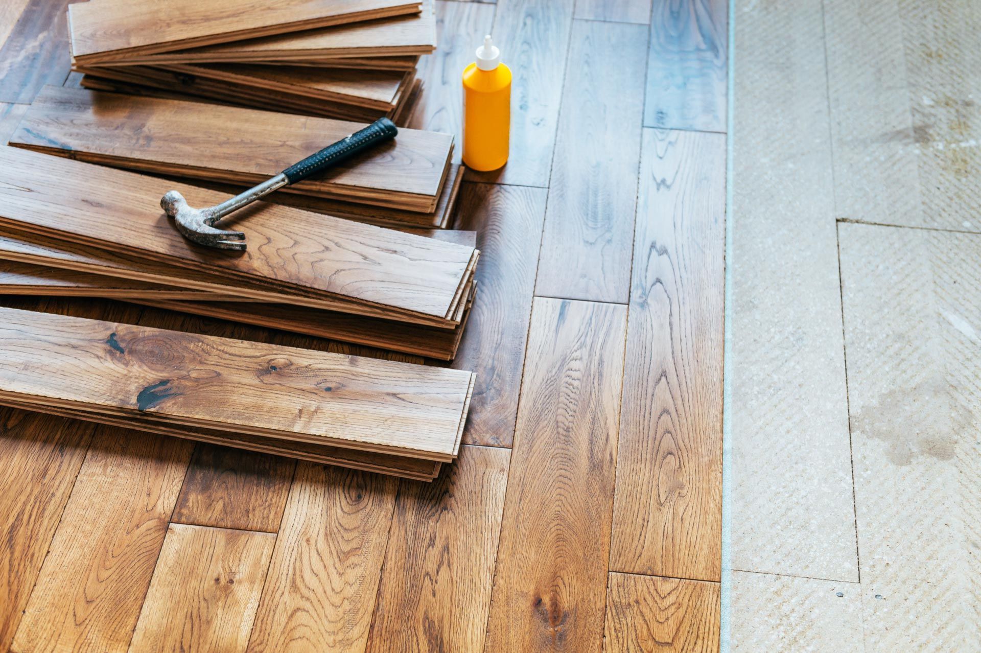 A hammer and a bottle of glue are on a wooden floor.