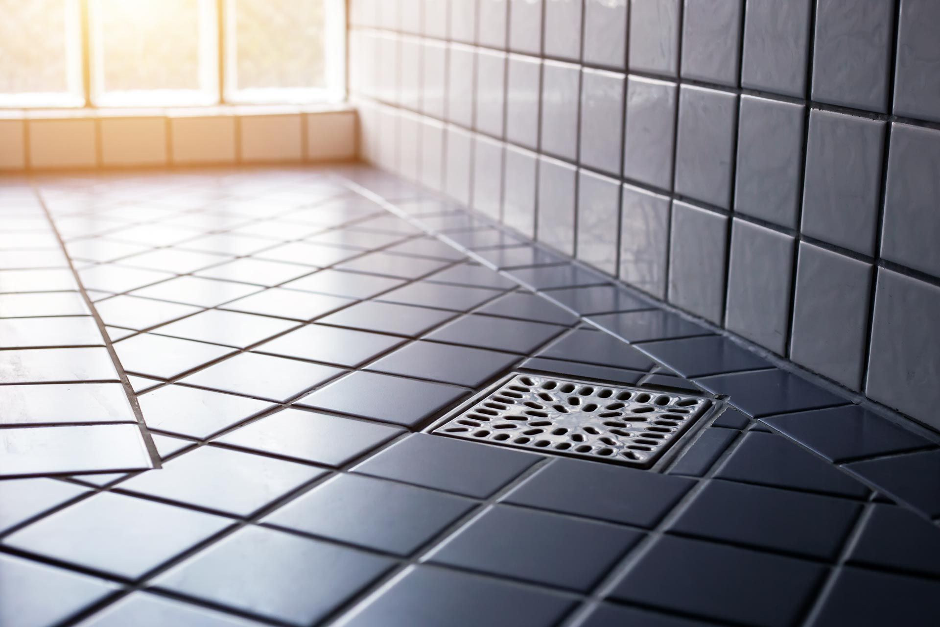 A close up of a tiled floor in a bathroom with a drain.