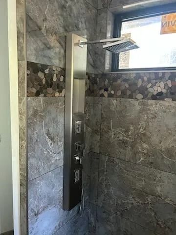 Modern walk-in shower with gray stone tile, black controls, and a rainfall showerhead