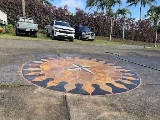 Round painted sun mosaic on pavement near parked vehicles and palm trees.