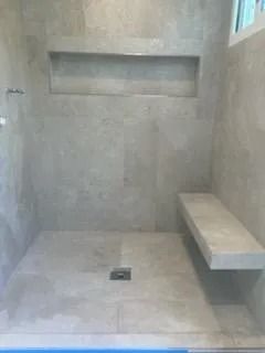 Small tiled shower with built-in bench and recessed wall shelf