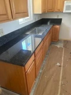 Kitchen with black granite countertop, wooden cabinets, and unfinished floor near a sink.