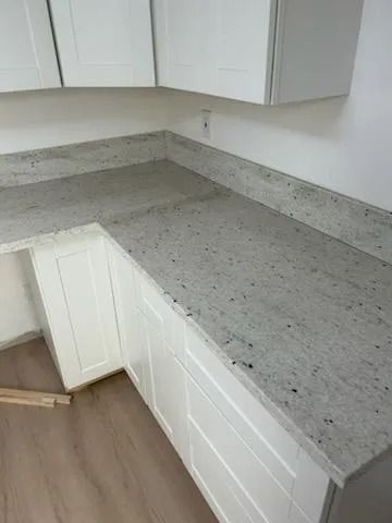 L-shaped kitchen countertop with gray speckled stone and white cabinets in a bright corner space
