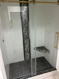 Glass shower enclosure with mosaic tile floor and built-in corner shelf