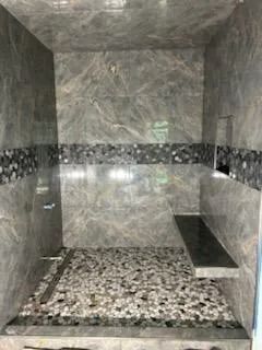 Stone-tiled shower stall with pebble floor and built-in bench
