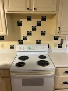 White electric stove in a beige kitchen with small black tile accents on the backsplash.