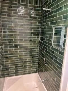 Empty shower with dark green tile walls and a pale tub basin, plus a small mirrored cabinet.