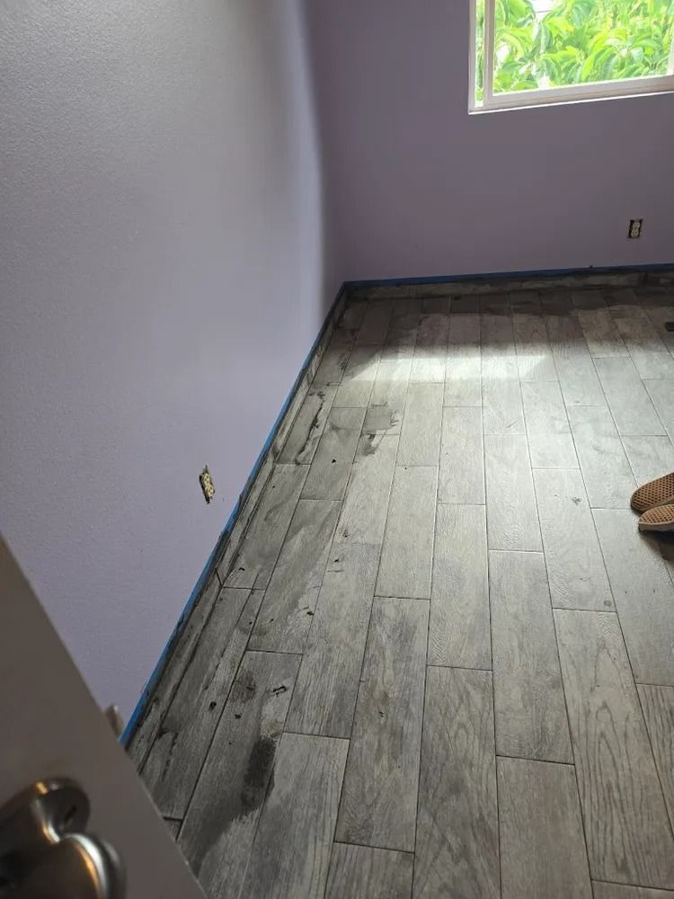 Empty room with gray walls, worn wood floor, and sunlight from a window.