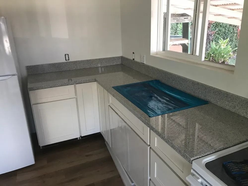 Small kitchen with granite countertops, white cabinets, window, sink, and stove.