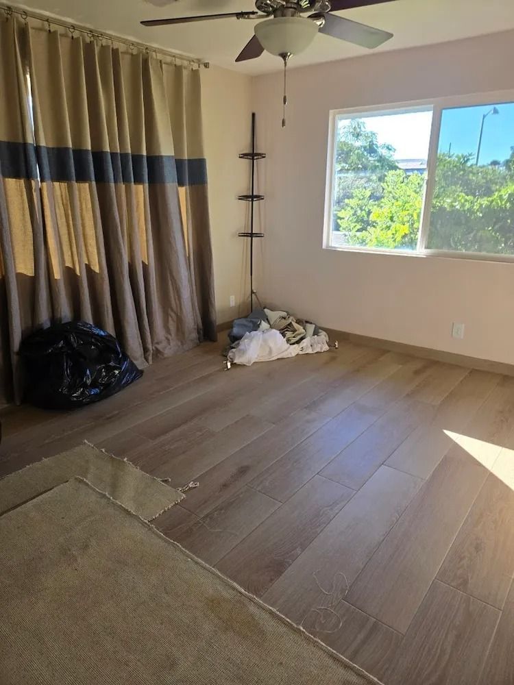 Empty unfurnished room with beige curtains, wood floor, and sunlight through a window