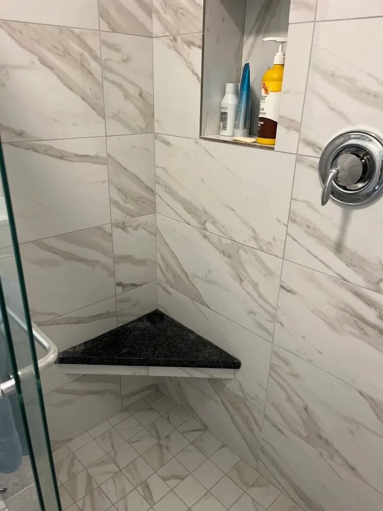 Small tiled shower with built-in corner shelf, wall niche, and chrome shower control.