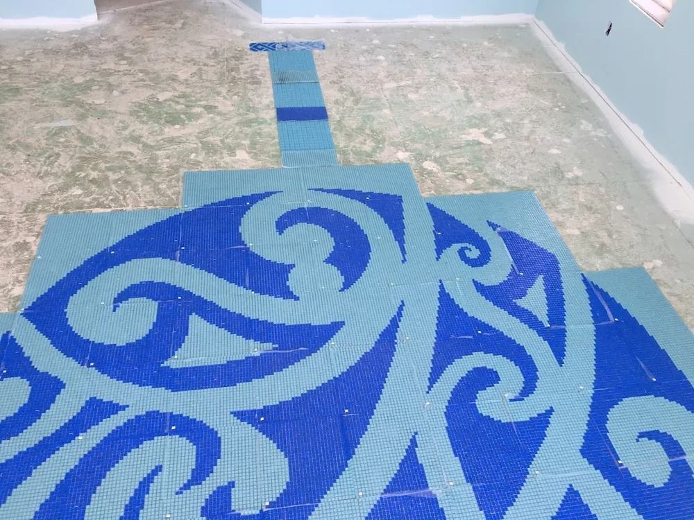 Blue-and-white decorative tiled mosaic on a floor, with swirling abstract patterns and a narrow walkway above