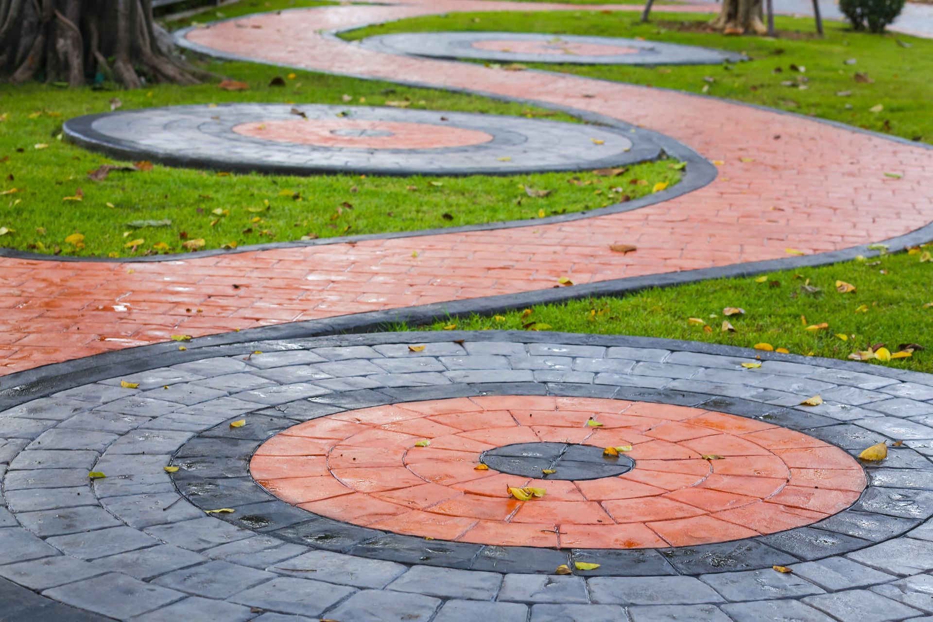 Circular brick and stone patterns in a park walkway, with green grass and trees nearby.