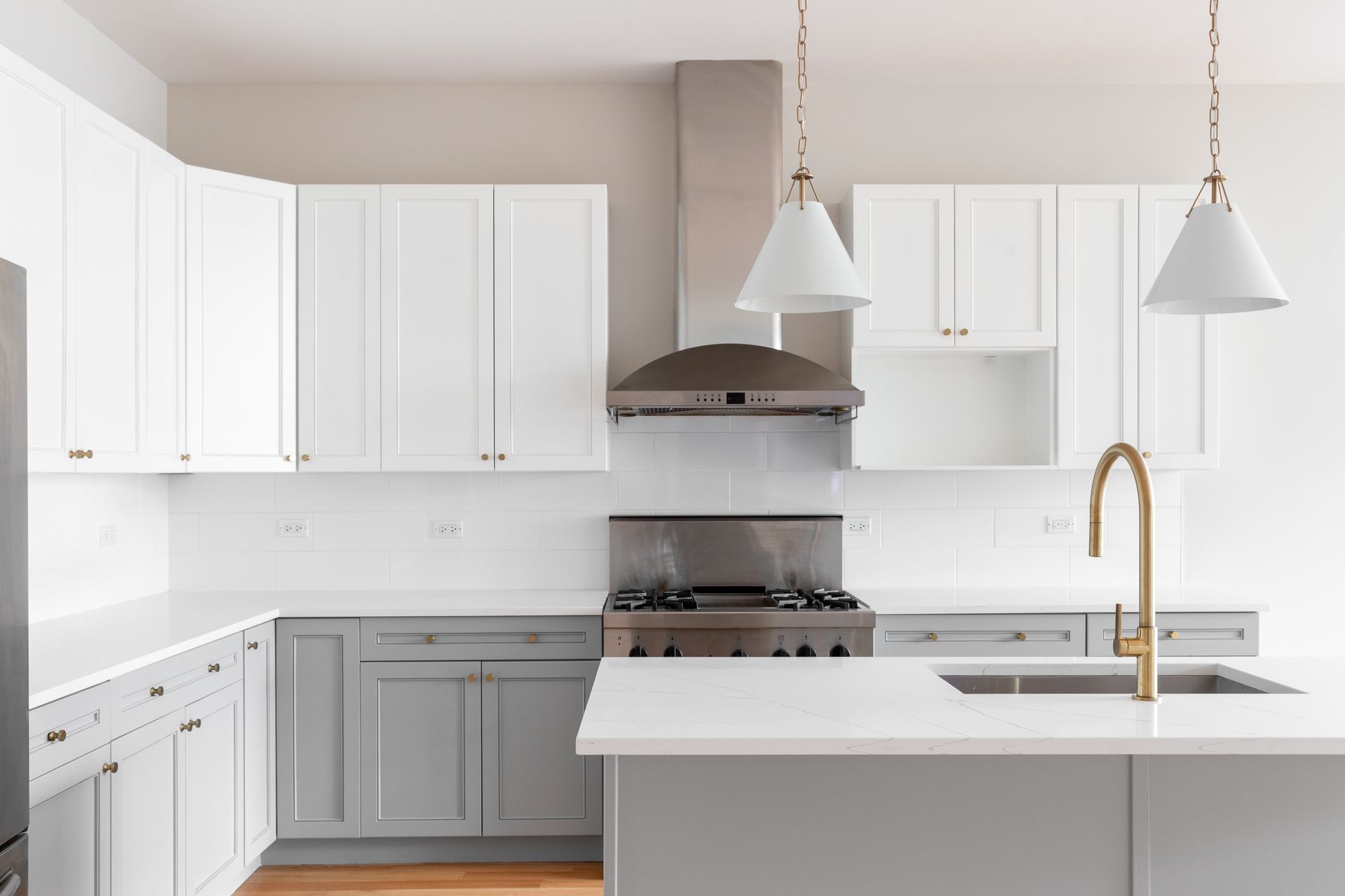 Modern gray kitchen with white island, stainless steel appliances, pendant lights, and wood floors