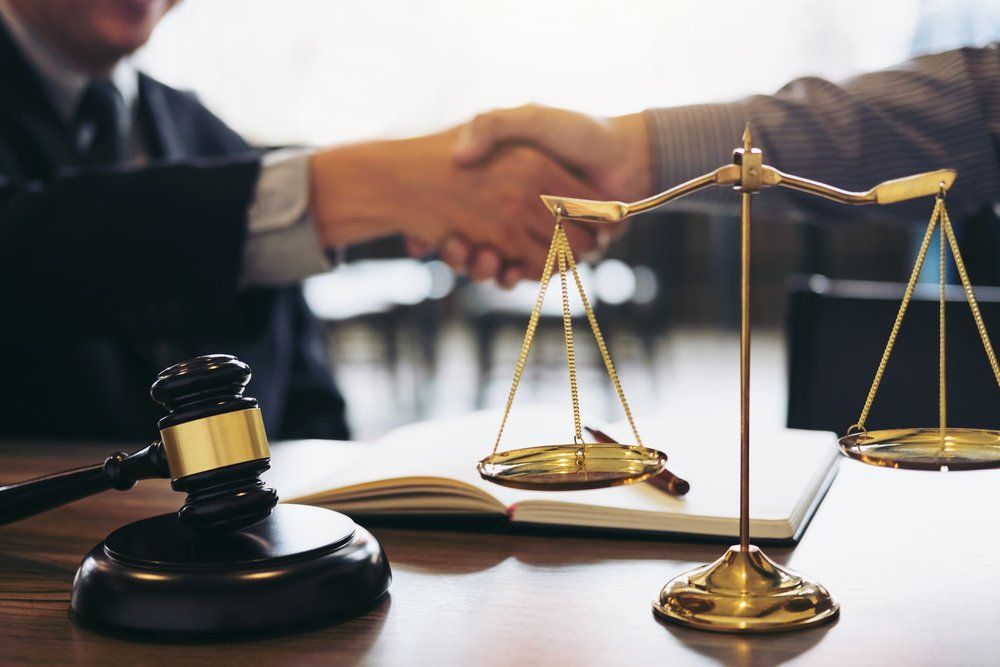 Lawyer And Client Shaking Hands Behind Justice Scales — Cairns Traffic Lawyers  in Cairns, QLD