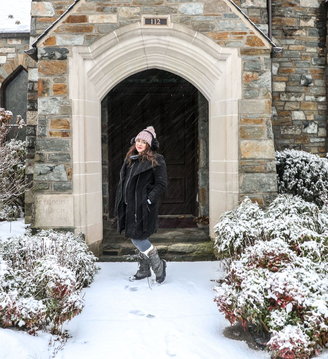 Woman in winter coat and hat stands in snowy doorway.