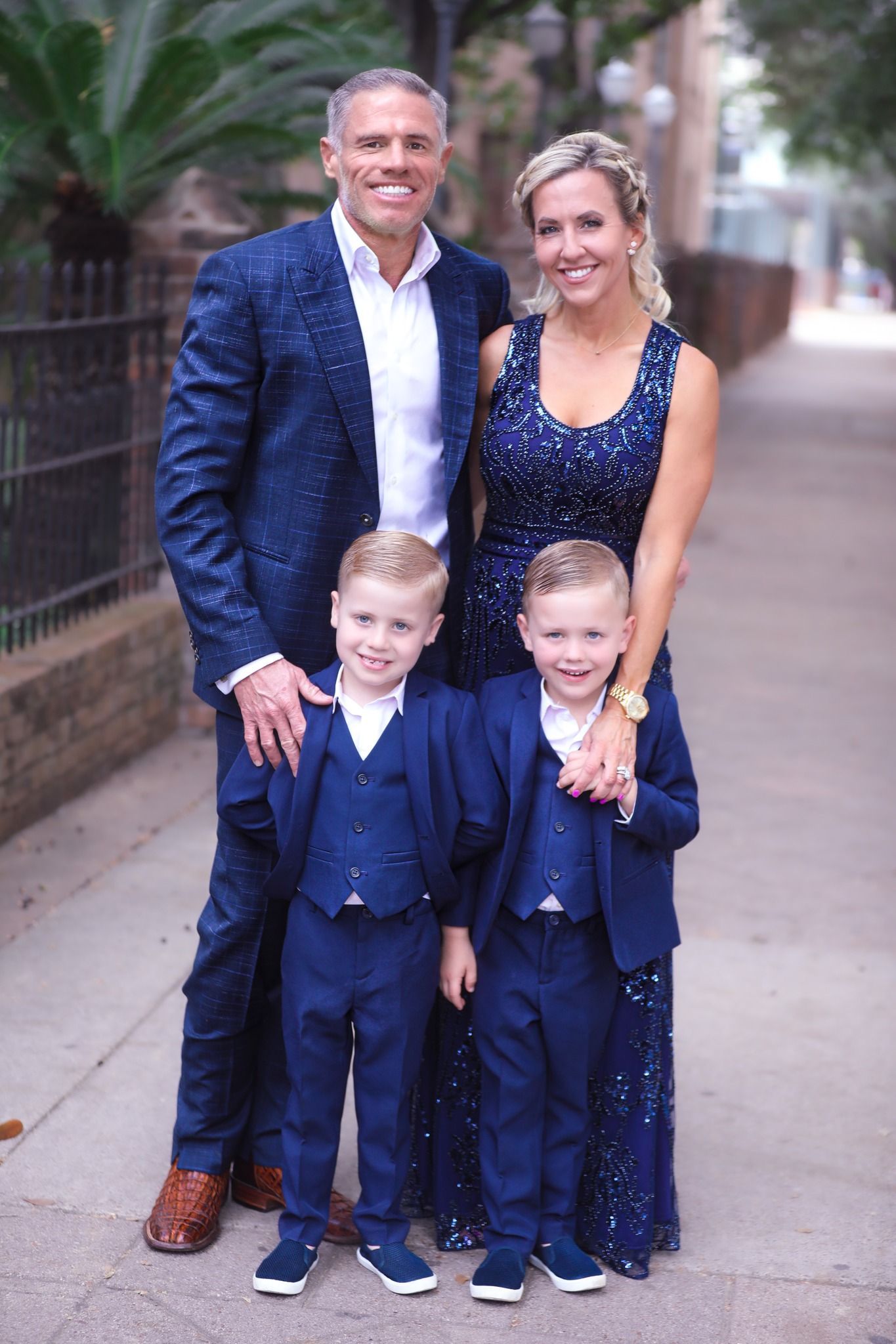 Family of four posing outdoors; parents and sons in matching blue outfits.