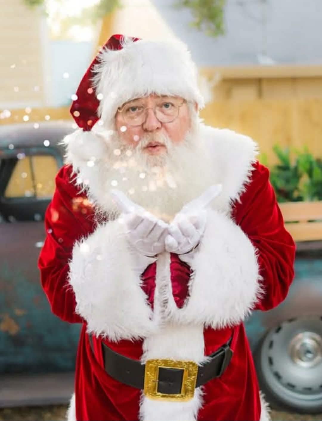 Santa Claus in red suit blowing sparkles, gold buckle, near a vintage truck.