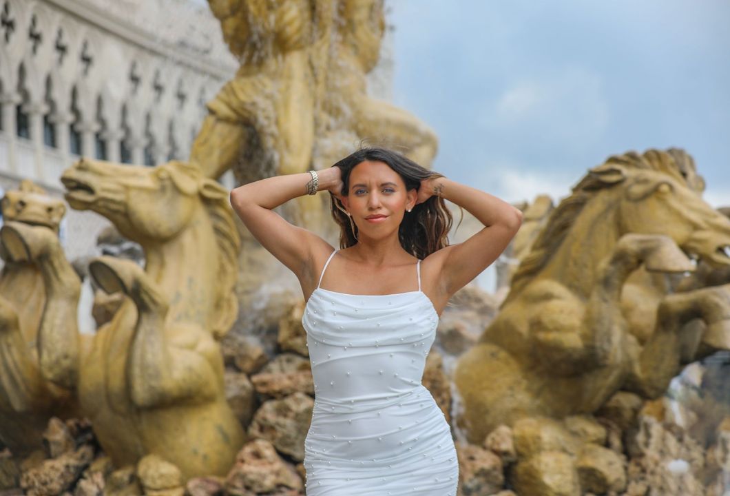 Woman in white dress posing by a Piazza San Marco sign, with patterned building in background.