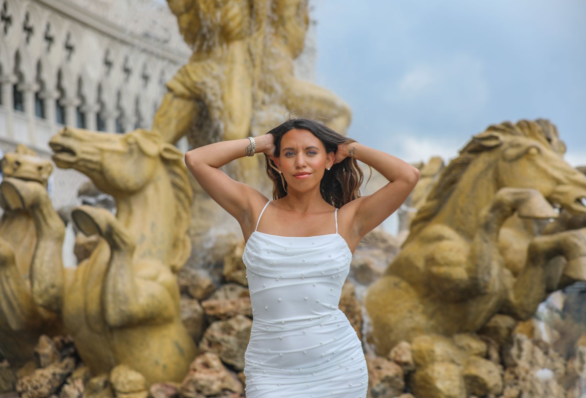 Woman in white dress posing by a Piazza San Marco sign, with patterned building in background.