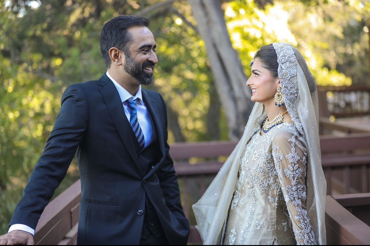 Couple gazing at each other on a wooden bridge; the man in a suit, the woman in a veil and ornate gown.