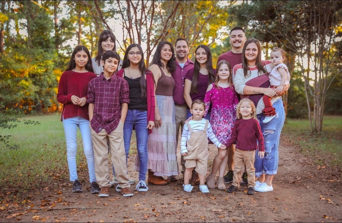 Family of 13 standing on a dirt path in a park, wearing various maroon and neutral-toned outfits.