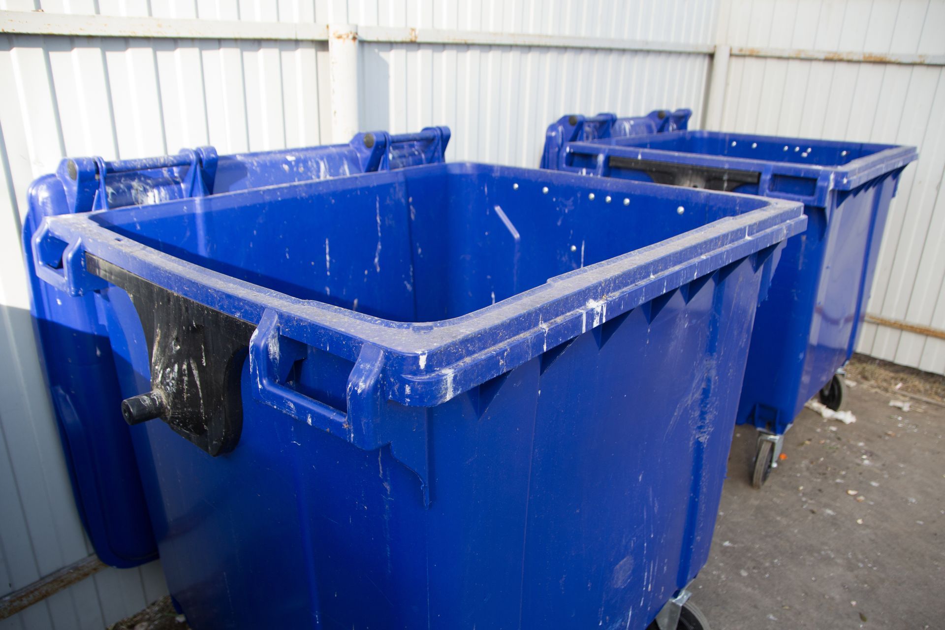 Three blue trash cans are sitting next to each other in front of a fence.