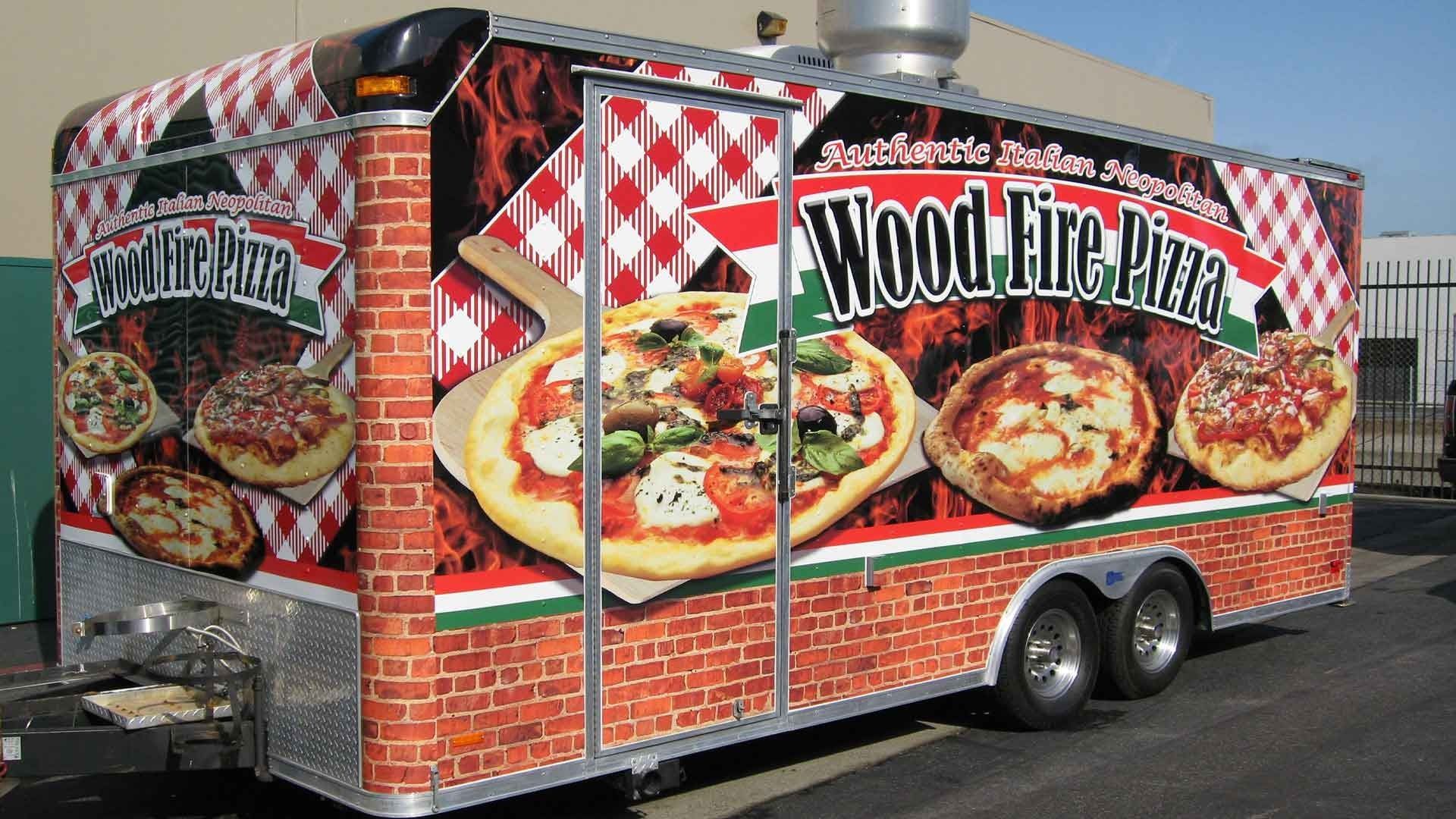 A food trailer featuring a red-and-white checkered pattern, brick-style siding, and photos of wood-fired pizzas.