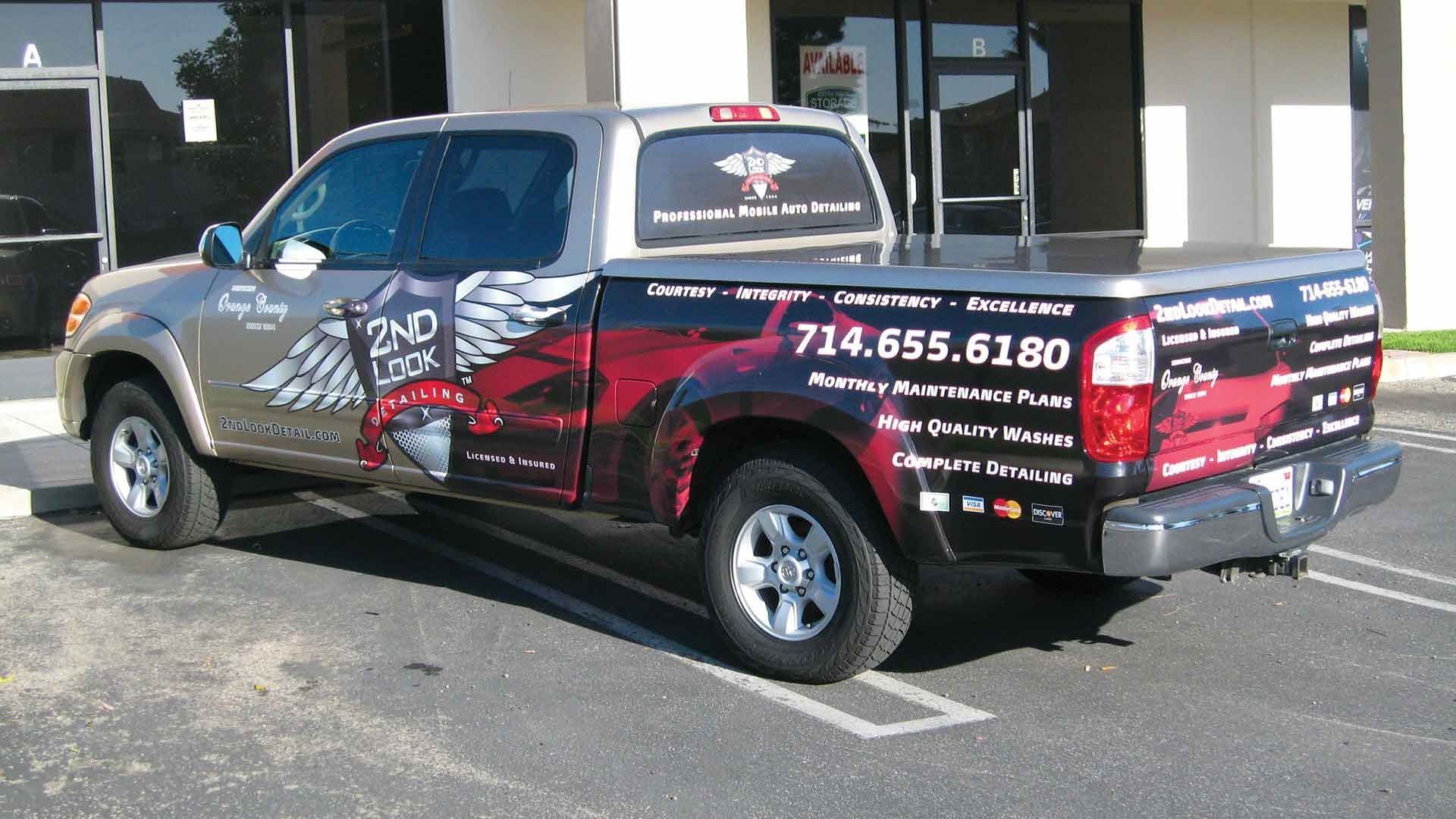 A silver and black pickup truck with 2nd Amendment-themed graphics parked outside a commercial building.