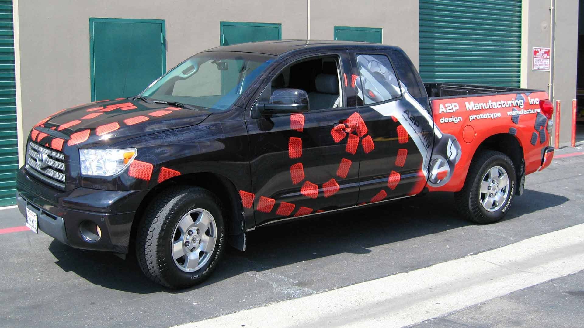 A black pickup truck parked in front of a building, decorated with red geometric shapes and a large white graphic.