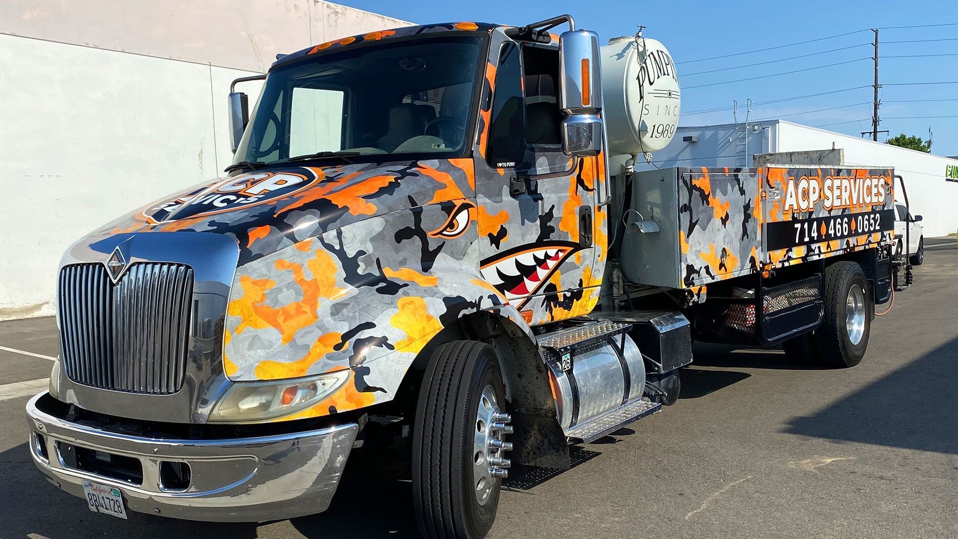 An International truck with an orange and gray camouflage wrap featuring shark teeth art, parked outdoors.