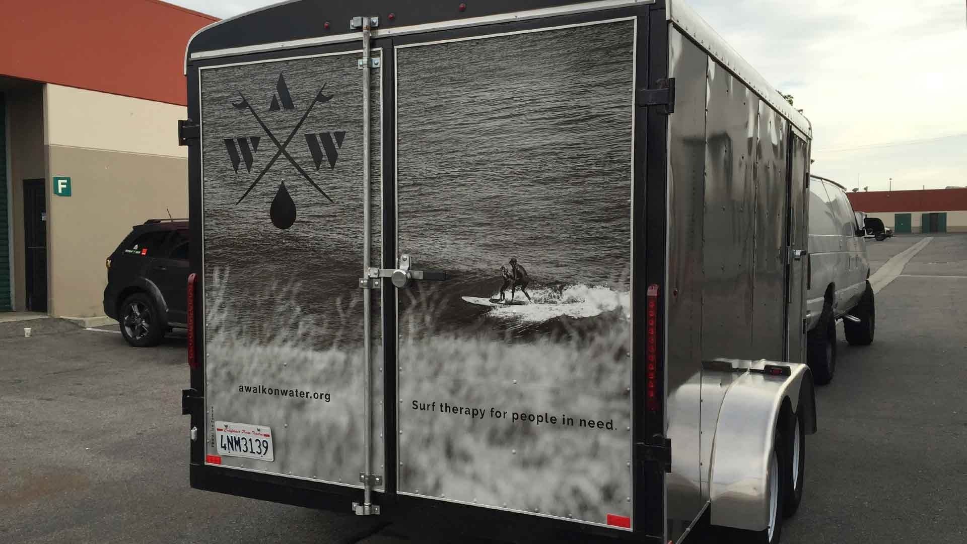 A black-and-white graphic wrap on the back doors of a parked utility trailer featuring a logo and outdoor scenery.