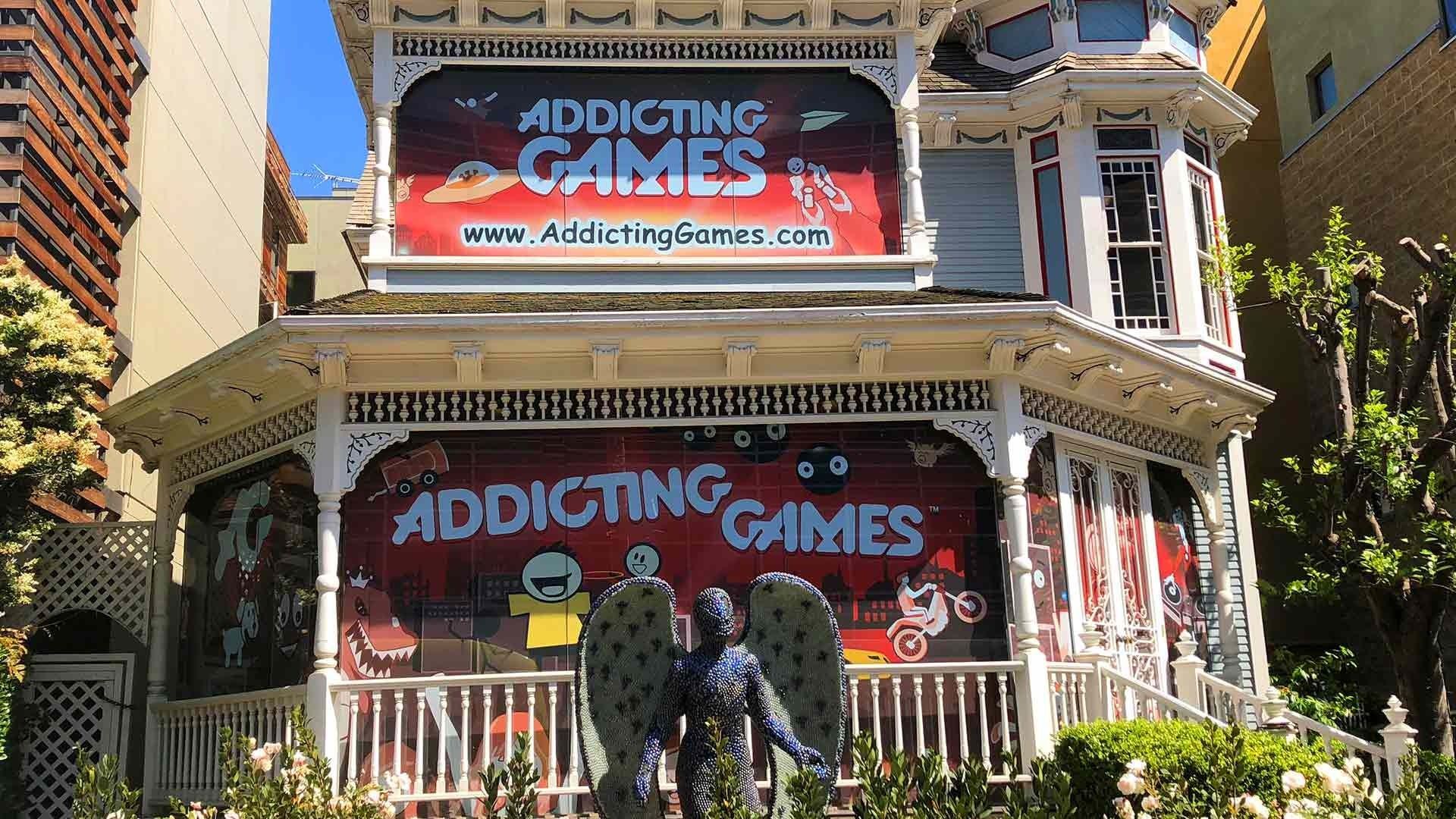 A Victorian house draped in red Addicting Games banners, featuring a prominent, wing-clad statue on the porch.
