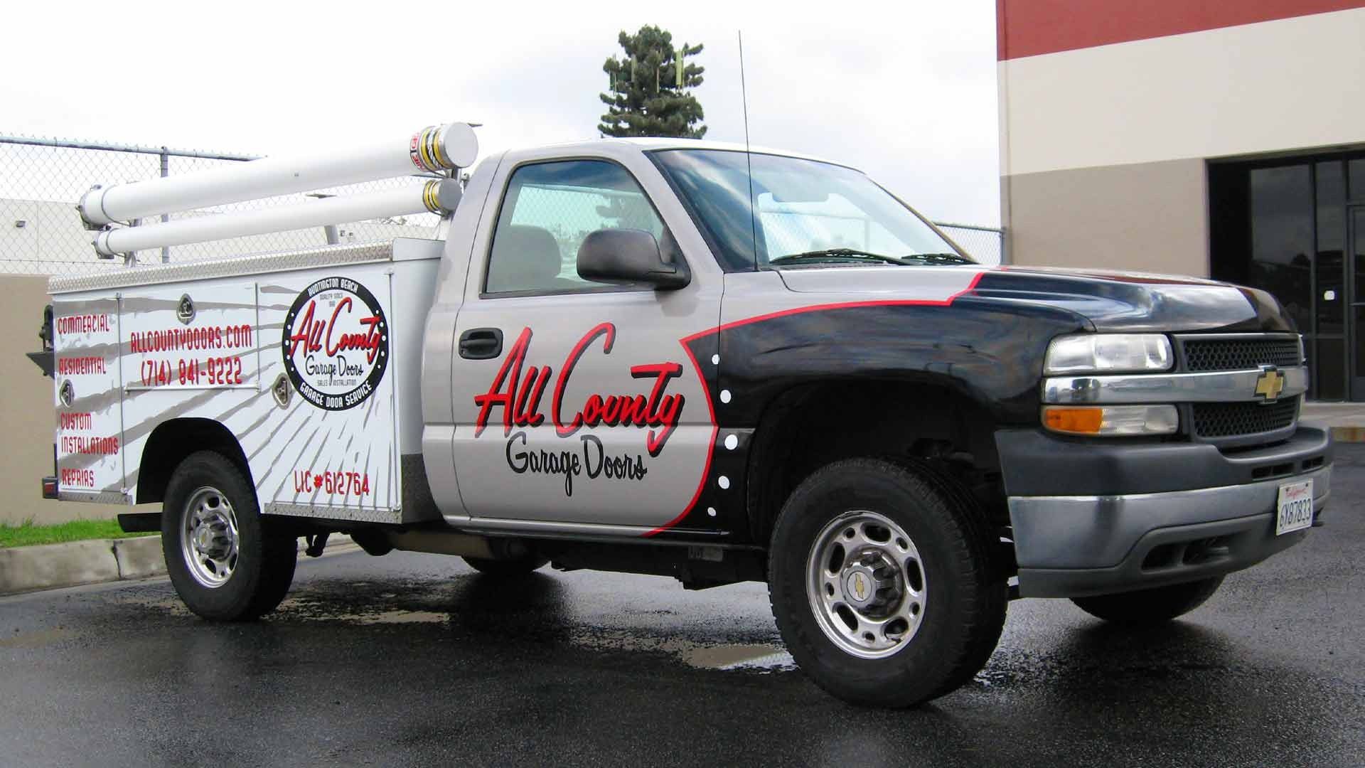A silver and black All County Garage Doors service truck parked on pavement.