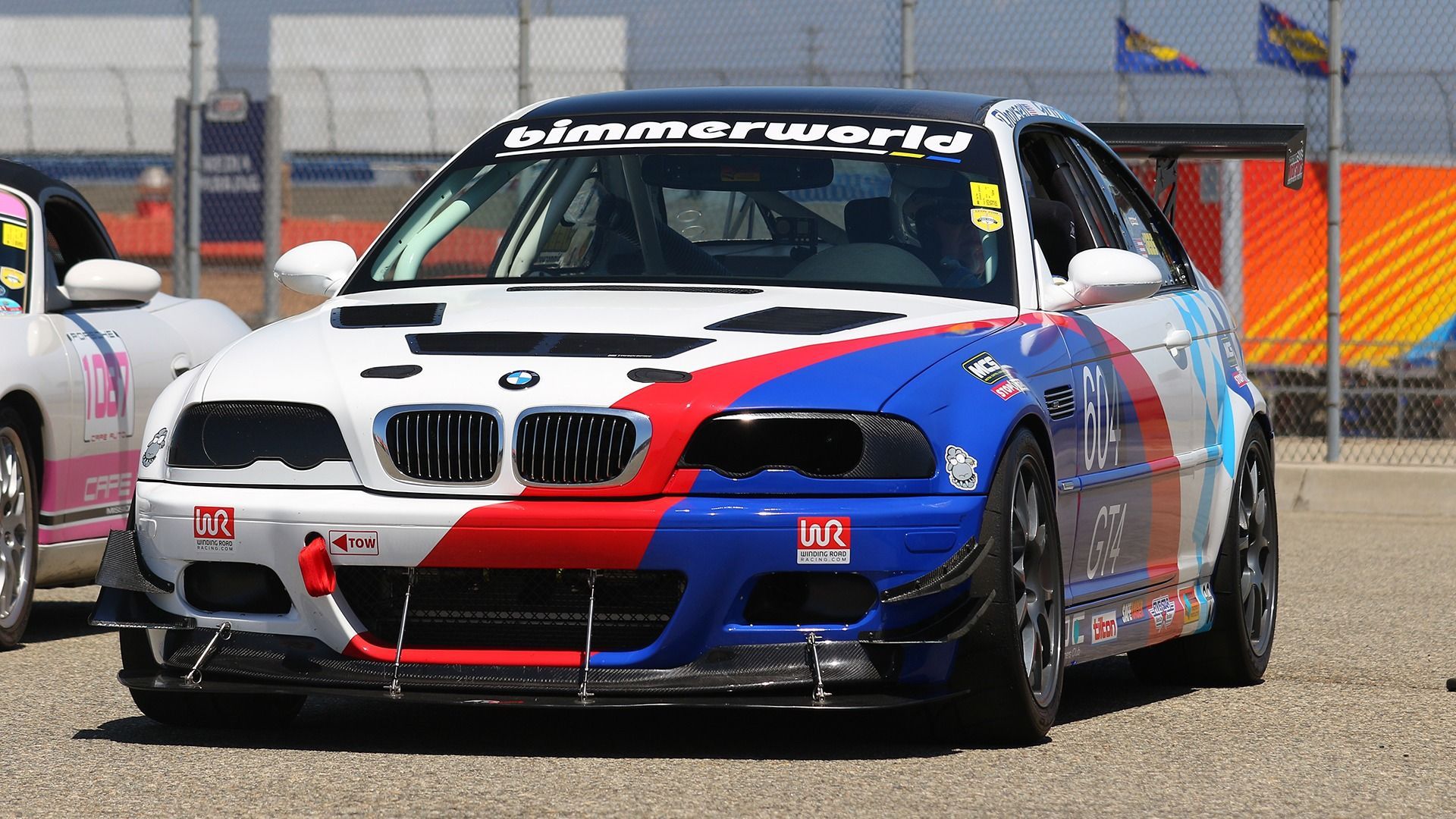 A white BMW E46 race car with blue and red livery and a 