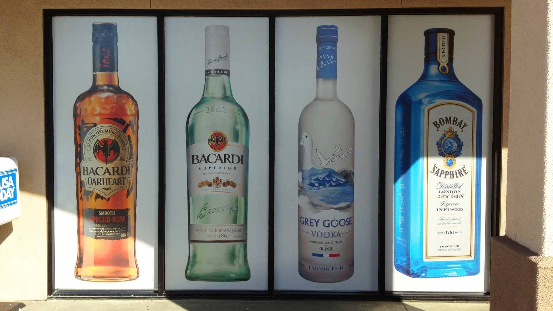 Four large window decals of liquor bottles: Bacardi Black, Bacardi Superior, Grey Goose vodka, and Bombay Sapphire gin.